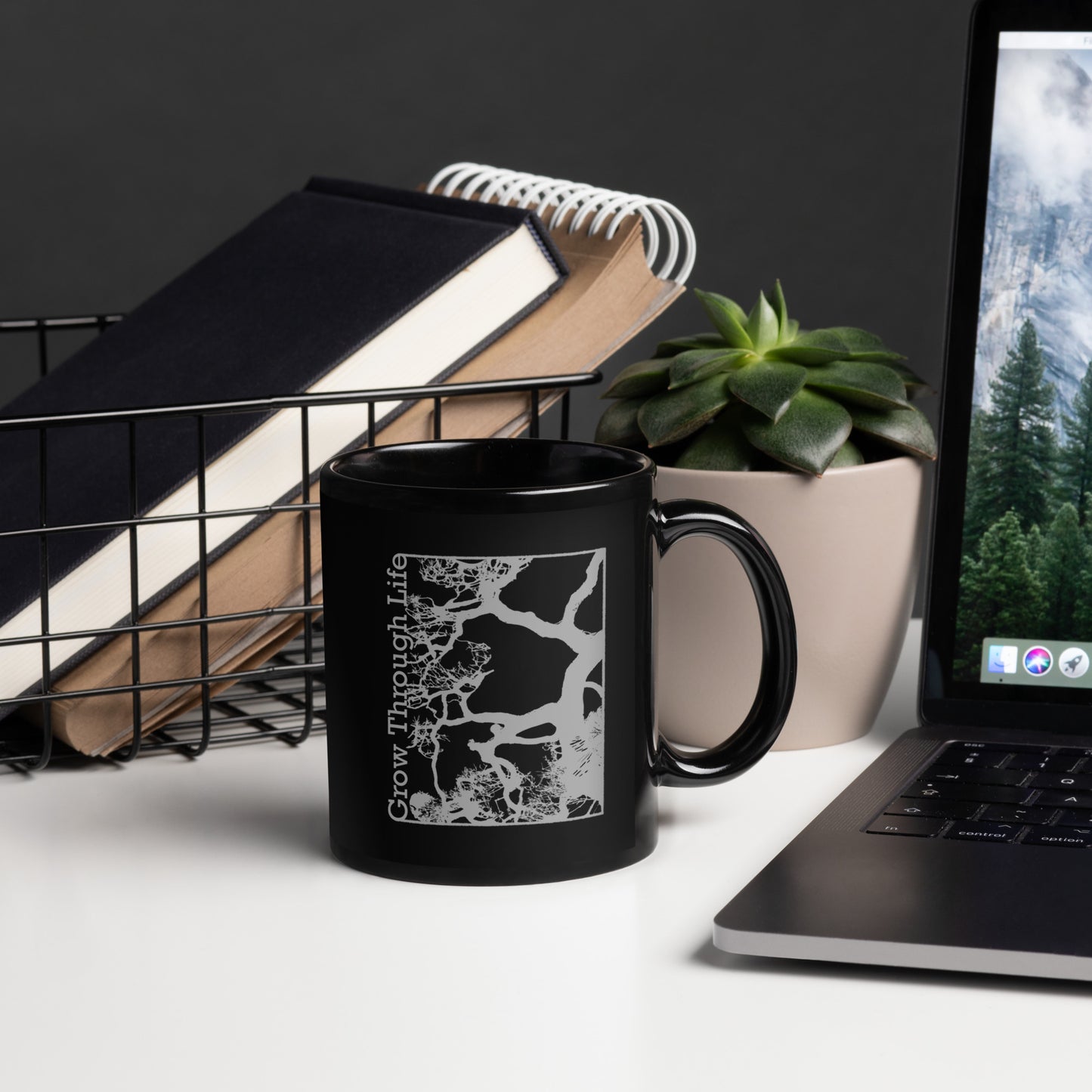 Black mug with light gray symbolic tree design, inspirational nature-themed drinkware. Desk View.