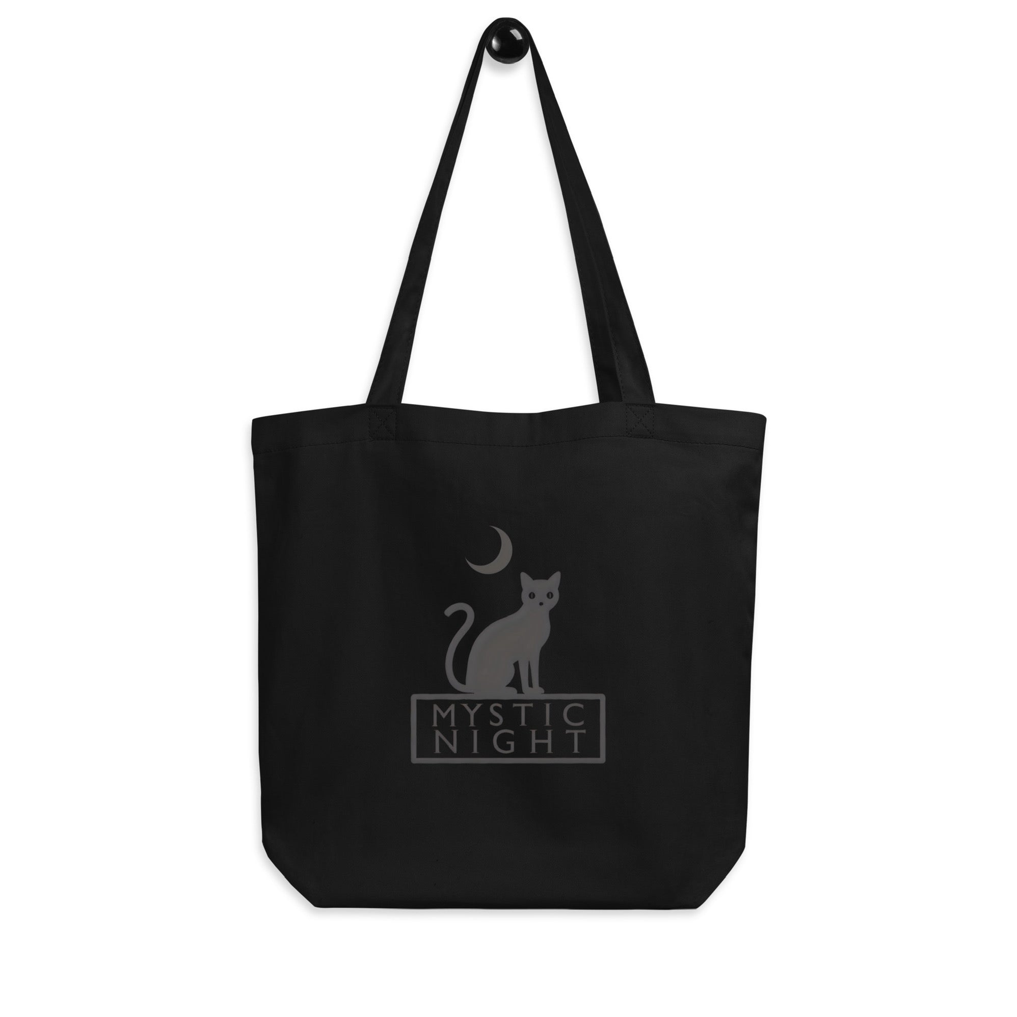 Minimalist black tote bag featuring a black cat sitting under a crescent moon with the text “Mystic Night” printed on beige and black backgrounds.