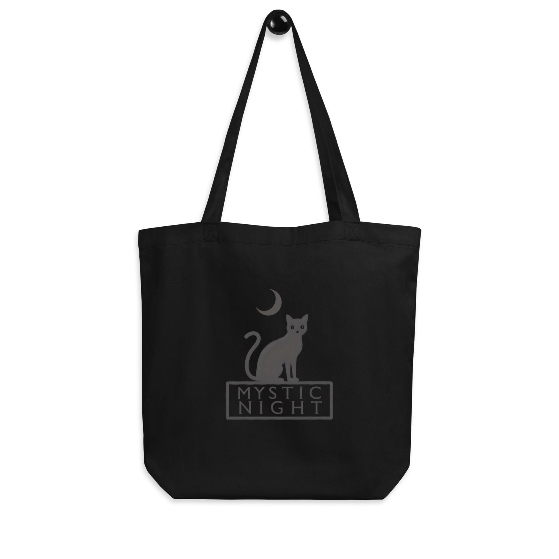 Minimalist black tote bag featuring a black cat sitting under a crescent moon with the text “Mystic Night” printed on beige and black backgrounds.